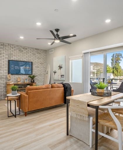 Living room with white and gray brick accent wall, hard flooring, recess lighting, ceiling fan, and sliding glass doors.