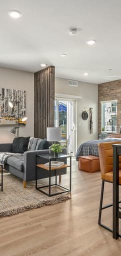 Open floorplan with light grey walls and a red brick accent wall, hard flooring, recess lighting, and windows.