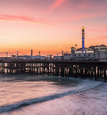 A pier with a Ferris wheel and a lighthouse at sunset.