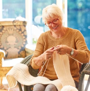an older woman sitting in a chair knitting a scarf