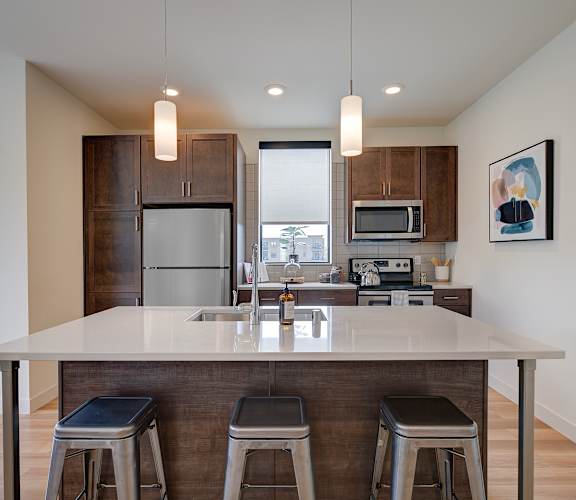 A kitchen with a white island and bar stools. at Statesman Apartments, Franklin, WI