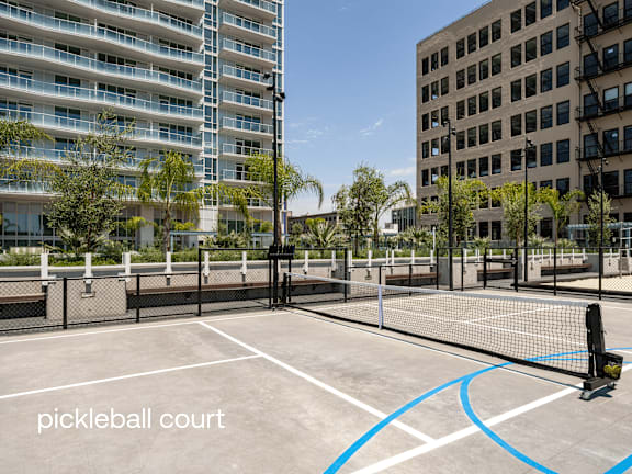 A pickleball court is surrounded by a fence and buildings. at Olympic + Hill Apartments, Apartments, Los Angeles, CA