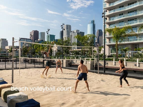 A beach volleyball court with players in action and a city skyline in the background. at Olympic + Hill Apartments, Apartments, Los Angeles, CA