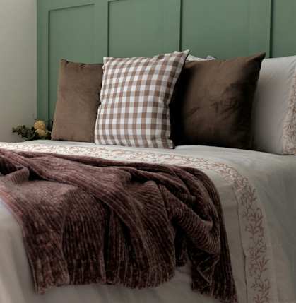A bed with a white comforter and a brown blanket.