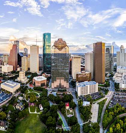 A cityscape with a mix of modern and older buildings, surrounded by greenery and roads.