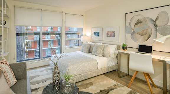 A modern bedroom with a large bed, a desk with a laptop, and a chair.