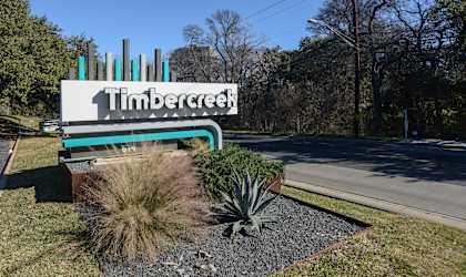 A sign that says Timbercreek in front of a grassy area.