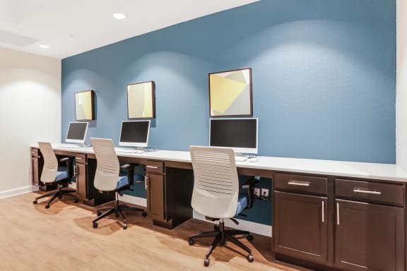 a row of computers on a long desk with three chairs in front of them