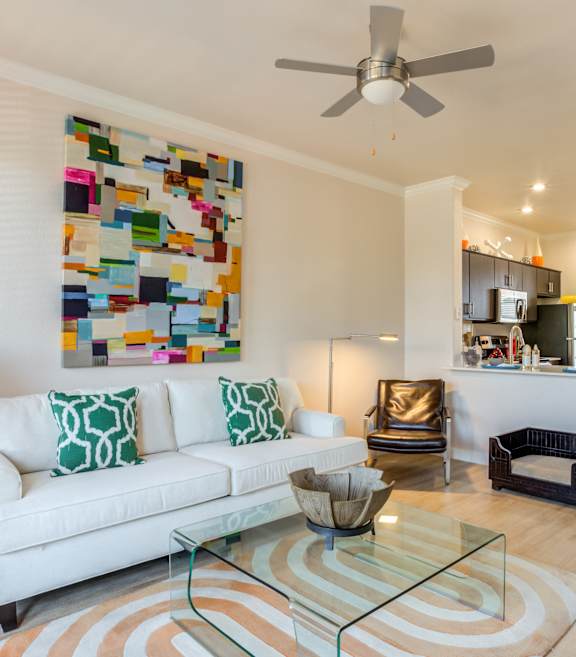 A living room with a white couch and a colorful wall hanging.
