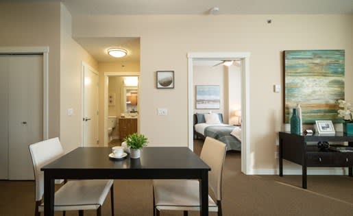 a dining room with a table and chairs and a bedroom in the background