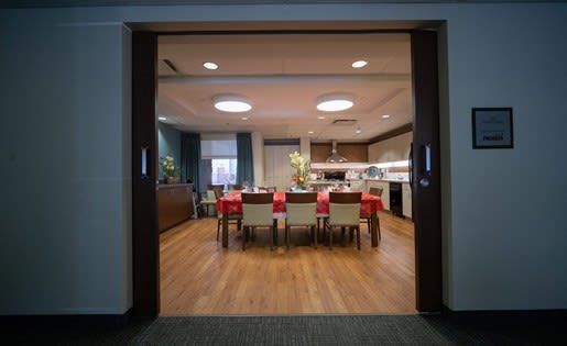 a room with a table and chairs and a kitchen in the background