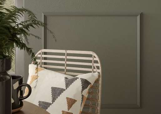 A chair with a quilt on it is in front of a grey wall.