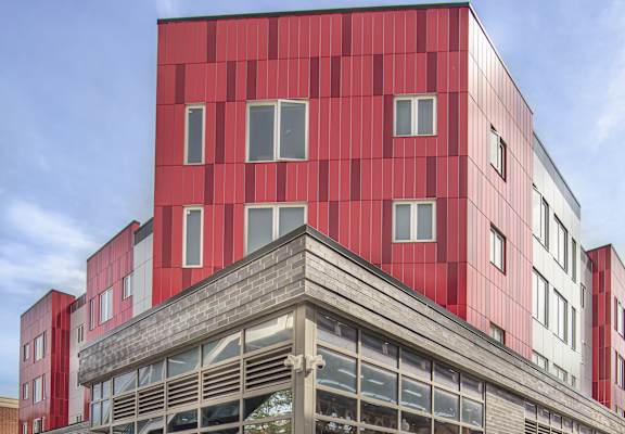A red building with a large glass front and people walking in front.