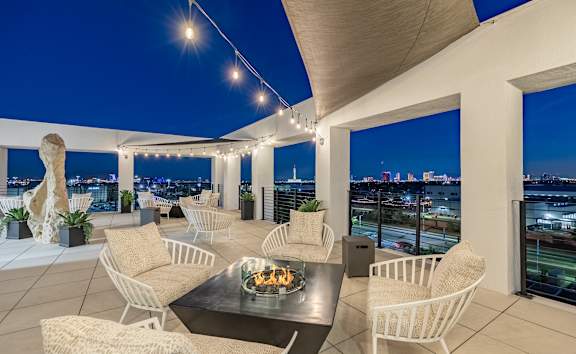 An outdoor rooftop residential lounge with chairs, tables, and overhead lights at theApex @ Meadows luxury apartments in Las Vegas, NV.