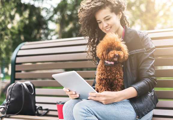 a woman sitting on a bench holding a dog and looking at a tablet