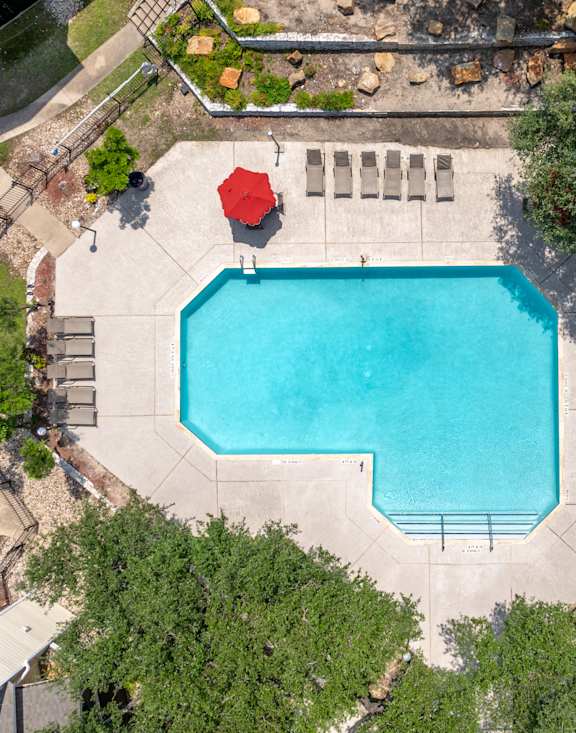 A red umbrella is on the edge of a blue swimming pool.
