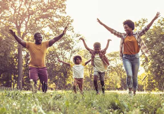 A family of four is running and jumping in a field.