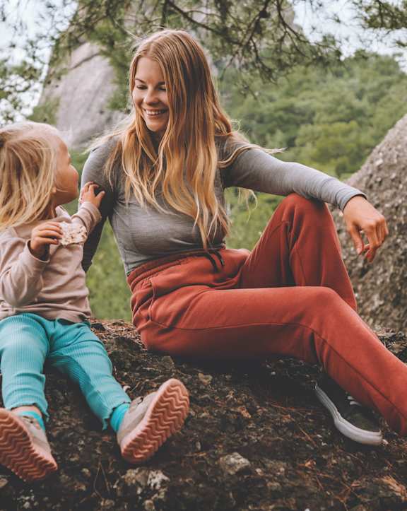 A woman and a child are sitting on a rock in a forest.