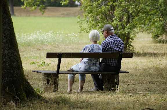 An elderly couple sits on a bench in a park.