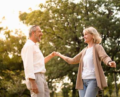 A man and a woman are holding hands and dancing in a park.
