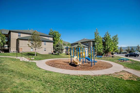 A playground with a yellow slide in the middle of a grassy area.