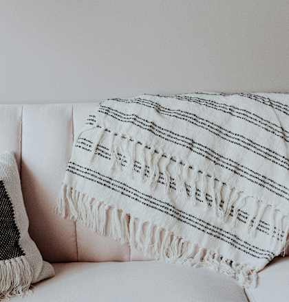 A white couch with a black and white pillow and a white and black striped blanket.
