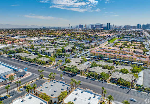 A cityscape with buildings, roads, and palm trees under a clear sky.