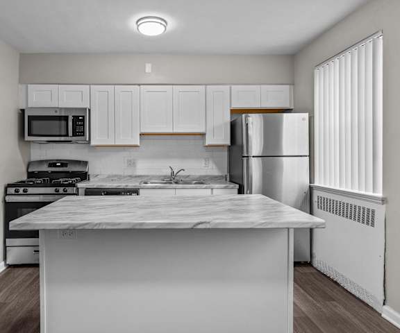 an empty kitchen with white cabinets and stainless steel appliances and a marble counter top
