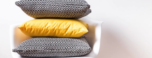Stock image of two gray and one yellow pillows stacked in a white chair