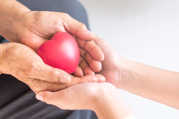 An elderly person is giving a red heart to a child.
