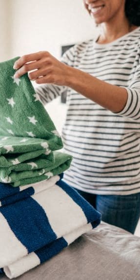a woman stacking a pile of towels on a bed