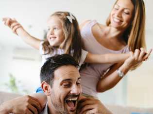 A man is holding a little girl on his shoulders while a woman stands behind them both.
