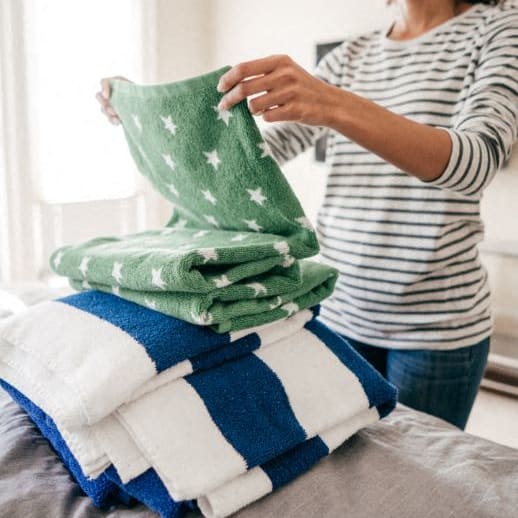 a woman stacking a pile of towels on a bed