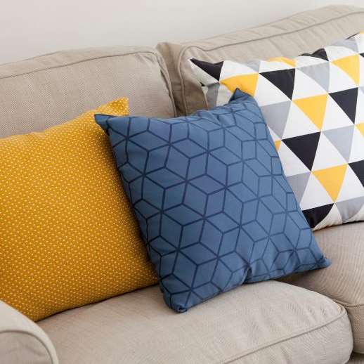 Three pillows on a beige couch with different patterns.