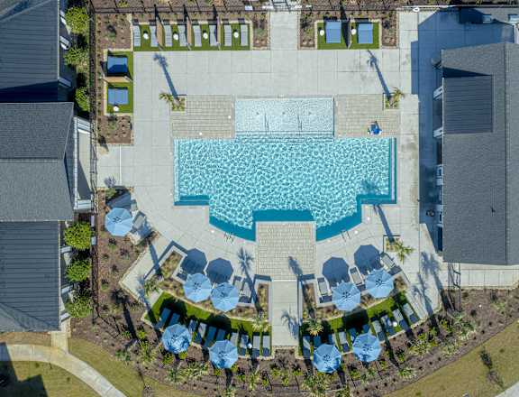 An aerial view of a swimming pool surrounded by a grassy area and buildings at Evolve St. James Apartment Homes Apartments, Southport, NC, 28461
