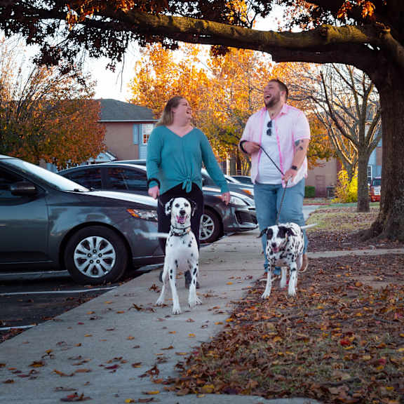 A couple walking two dogs on a leash on a sidewalk at Edgewood Estates Apartment Homes. 