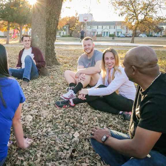 A group of people sitting in a circle in a park at Sonora Apartment Homes.