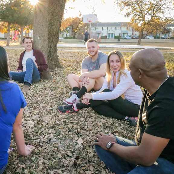 A group of people sitting in a circle in a park at Legacy West Apartment Homes.
