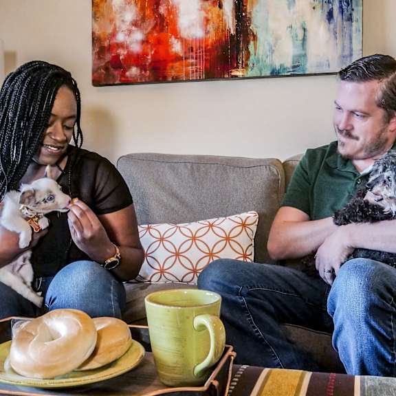 A couple sitting on a couch with their dogs at Cambridge West Apartment Homes.