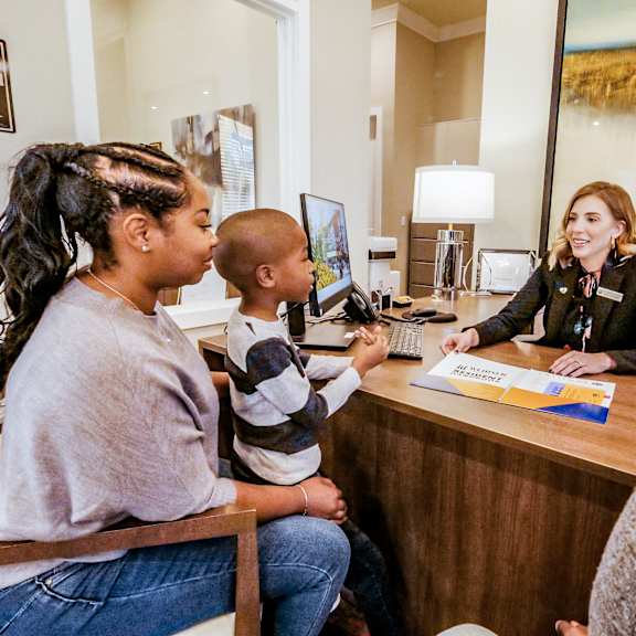 A woman sitting at a desk talking to a family at a reception desk at 3600 Brentwood Apartment Homes.
