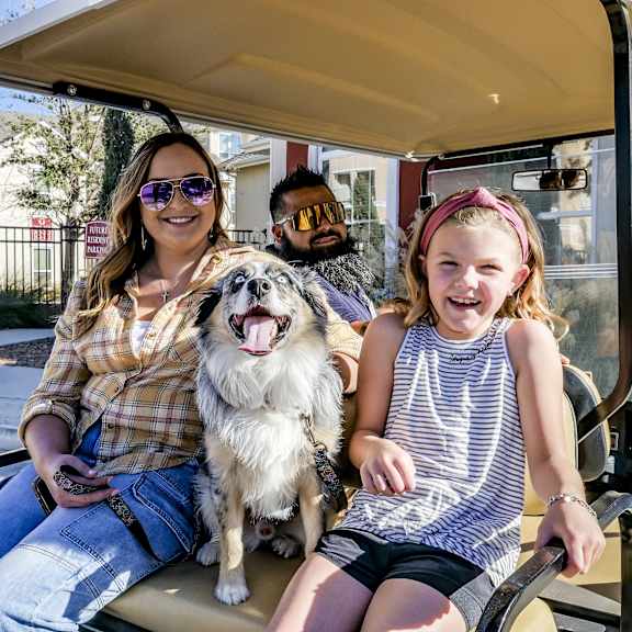 A man, a woman, and a child sitting in a golf cart with a dog at Hyde Park North. 