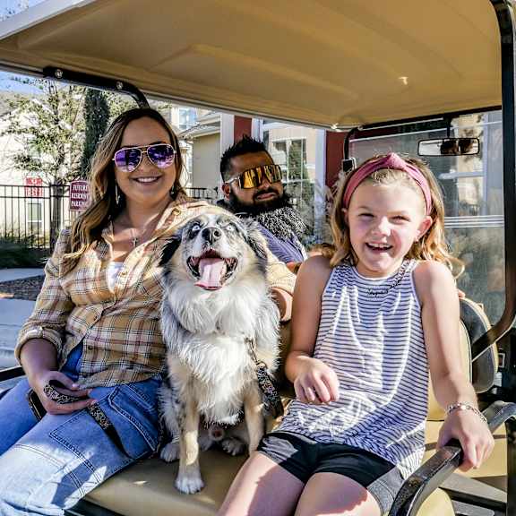 A woman, man, and child sitting in a golf cart with a dog at Chugach South Apartments.