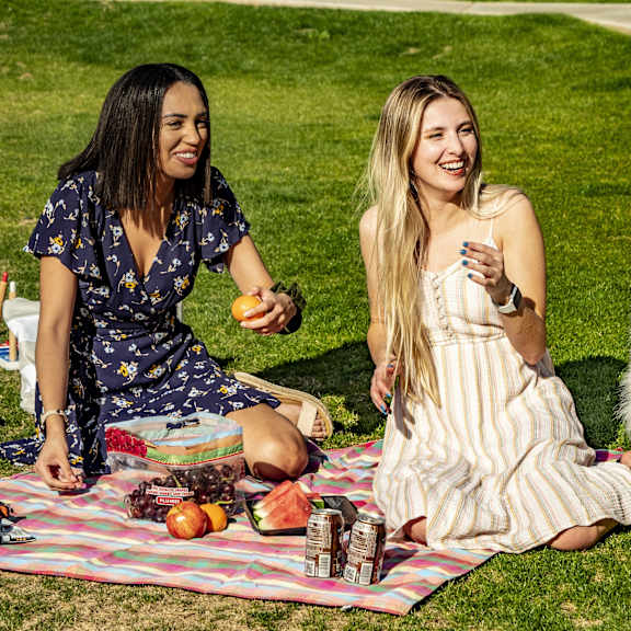 A group of people sitting on a picnic blanket with a dog at Dakota Apartments.
