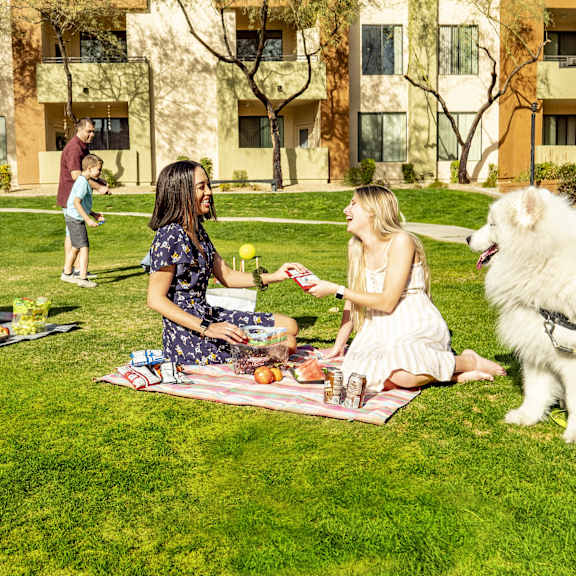 A group of people sitting on a lawn with a dog having a picnic at Wildwood Estates Apartment Homes.