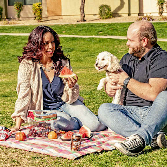 A man and woman sitting on a picnic blanket with their dog at Susitna Ridge Apartment Homes.