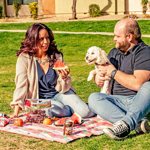 A man and woman sitting on a picnic blanket with their dog at Bristol Square. 