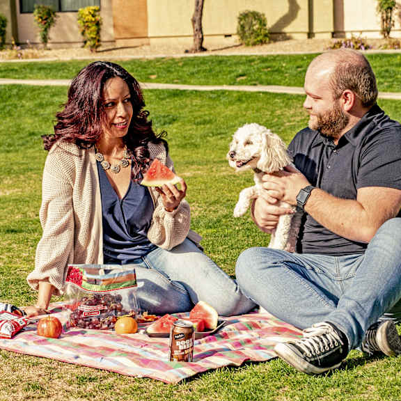 A man and woman sitting on a picnic blanket with their dog at Kingsmere Apartment Homes.