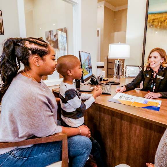 a woman sitting at a desk talking to two children at a reception desk