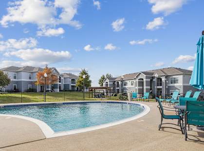 a swimming pool with chairs and umbrellas in front of apartment buildings