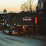 Two people walking down a street past a bar with a sign that says "Von Lee.".